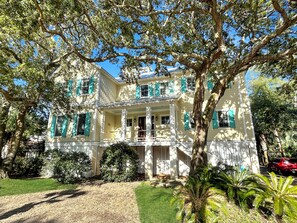 A two-story building with a porch, surrounded by trees and greenery.