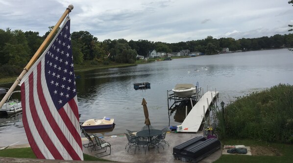 A lakeside dock with a flag, a boat, and a table with chairs. - Spacious Lake Home Close To Notre Dame (Edwardsburg)