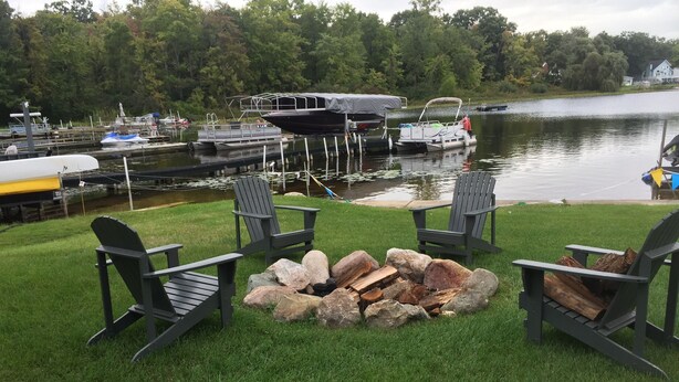 Terraza junto al lago con sillas Adirondack y un pozo de fuego.