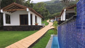 A pathway leading to a pool area with a blue tiled wall on one side and a white building with a brown roof on the other. - Villas Casteletes-bangalow Sea View (Velas)