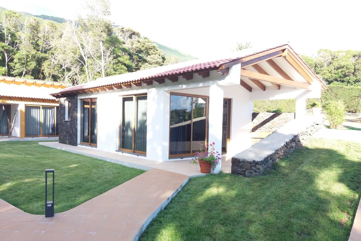 A modern house with a tiled roof, large sliding glass doors, and a stone retaining wall.