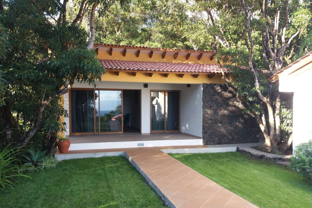 A modern house with a tiled roof, large sliding glass doors, and a well-maintained lawn.