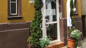 A yellow building with a brown door and windows. There are potted plants and a lantern on the porch. - Haus am Cannstatter Wasen (Stuttgart)