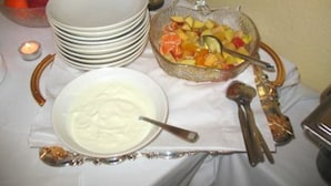 A table with a fruit bowl, a bowl of yogurt, and stacked plates. - Haus am Cannstatter Wasen (Stuttgart)