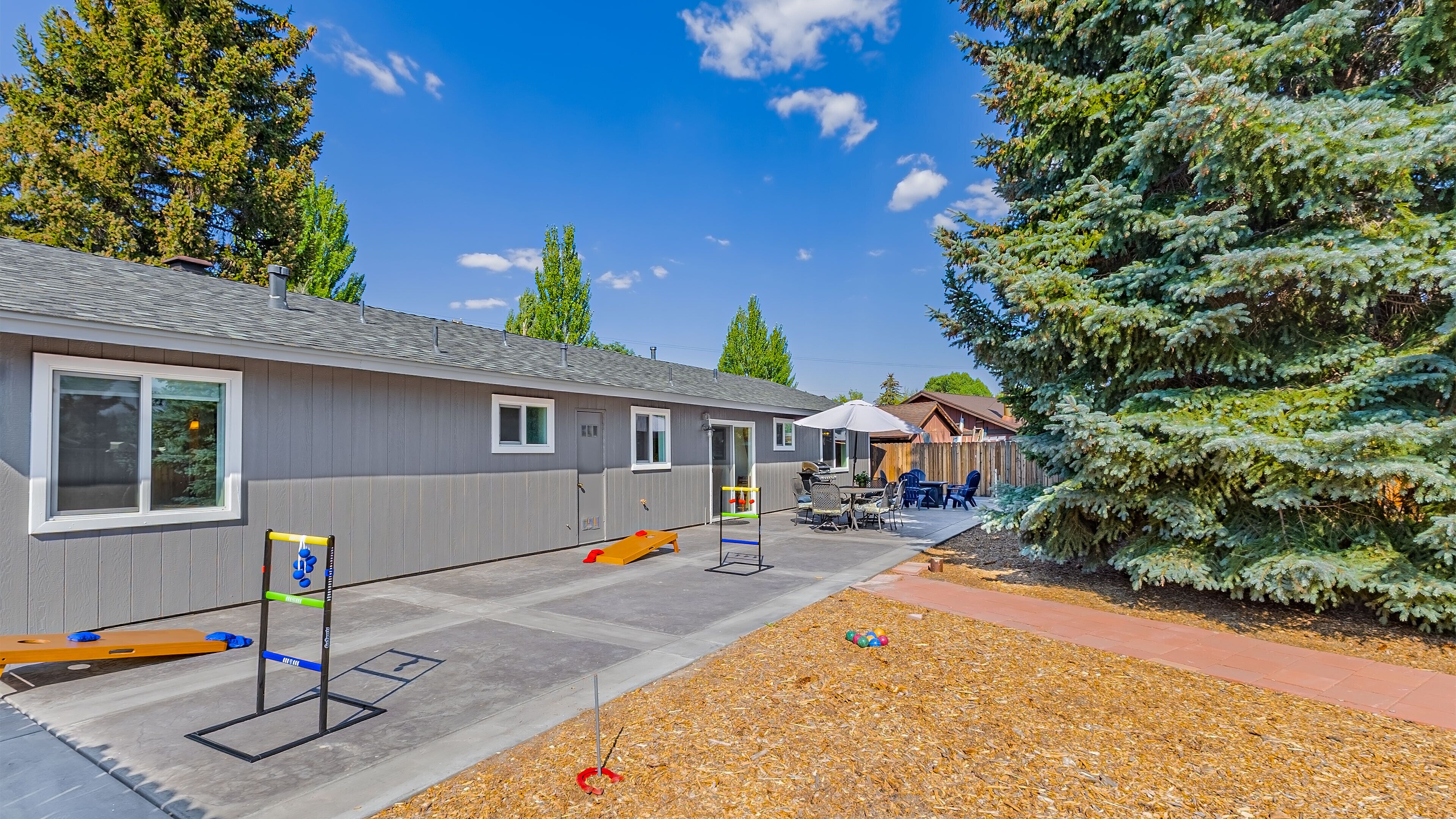 A row of cabins with a patio area, outdoor seating, and a large evergreen tree.