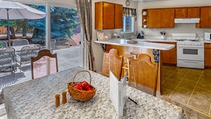 Una cocina con armarios de madera, encimera blanca y zona de comedor con sillas de mimbre.