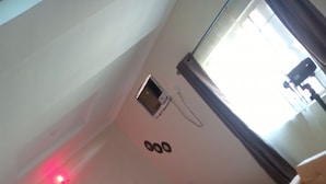 A hotel room with a bed, a small window, and a wall-mounted phone. - Jimson International Hotel and Suites (Abeokuta)