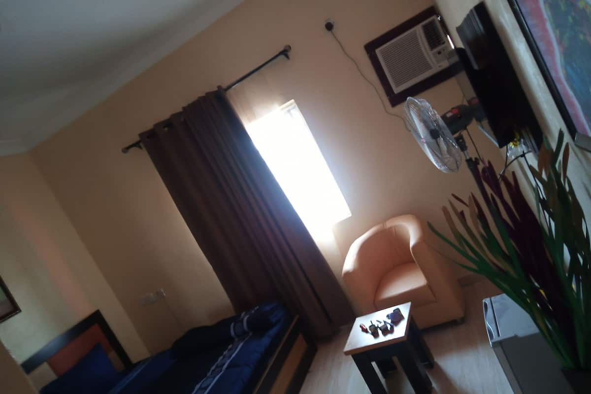 Een woonkamer met een bank, een bijzettafeltje, een stoel, een ventilator en een raam met gordijnen.
