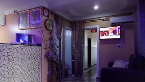 A living room with a television, a sofa, a decorative plant, and a tiled wall. - Jimson International Hotel and Suites (Abeokuta)