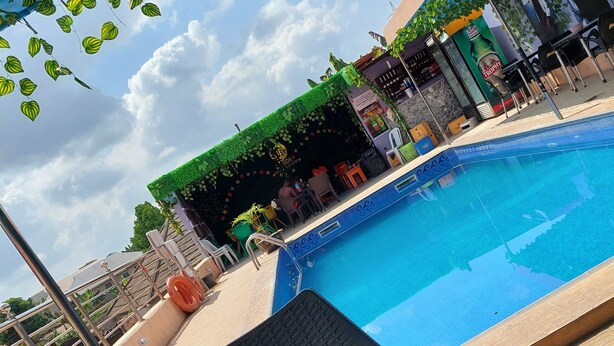 A swimming pool with a tiled edge, surrounded by lounge chairs and a covered area with greenery. - Jimson International Hotel and Suites (Abeokuta)