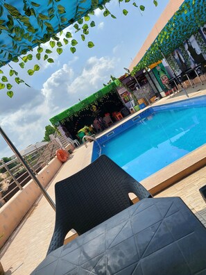 Una piscina con borde de azulejos, rodeada de sillas de descanso y una zona cubierta con vegetación.