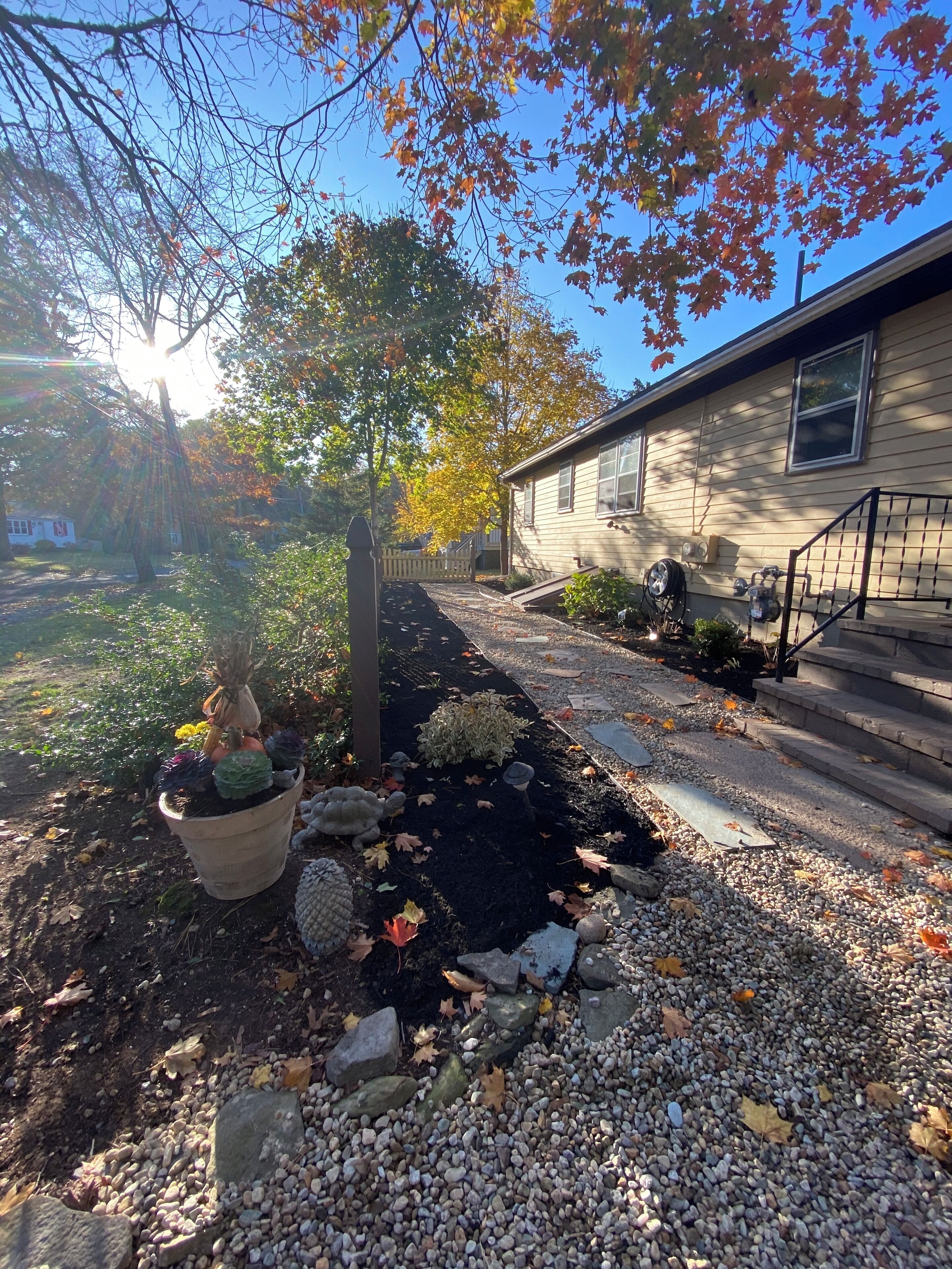 A pathway leading to a house with a gravel driveway, a wooden fence, and a variety of potted plants.