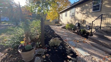 A pathway leading to a house with a gravel driveway, a wooden fence, and a variety of potted plants.