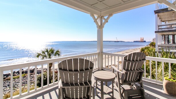 A covered outdoor area with two Adirondack chairs and a small table, overlooking a beach with a clear view of the ocean and a distant ship. - HIGH TIDE Ocean Front Beach Cottage, Best Views on St Simons Island! Pier Area! (Saint Simons Island)
