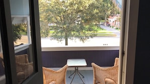 A balcony with wicker chairs, a small table, and a view of a tree-lined street. - 1887 Royellou House 3BR 2BA (Mt Dora)