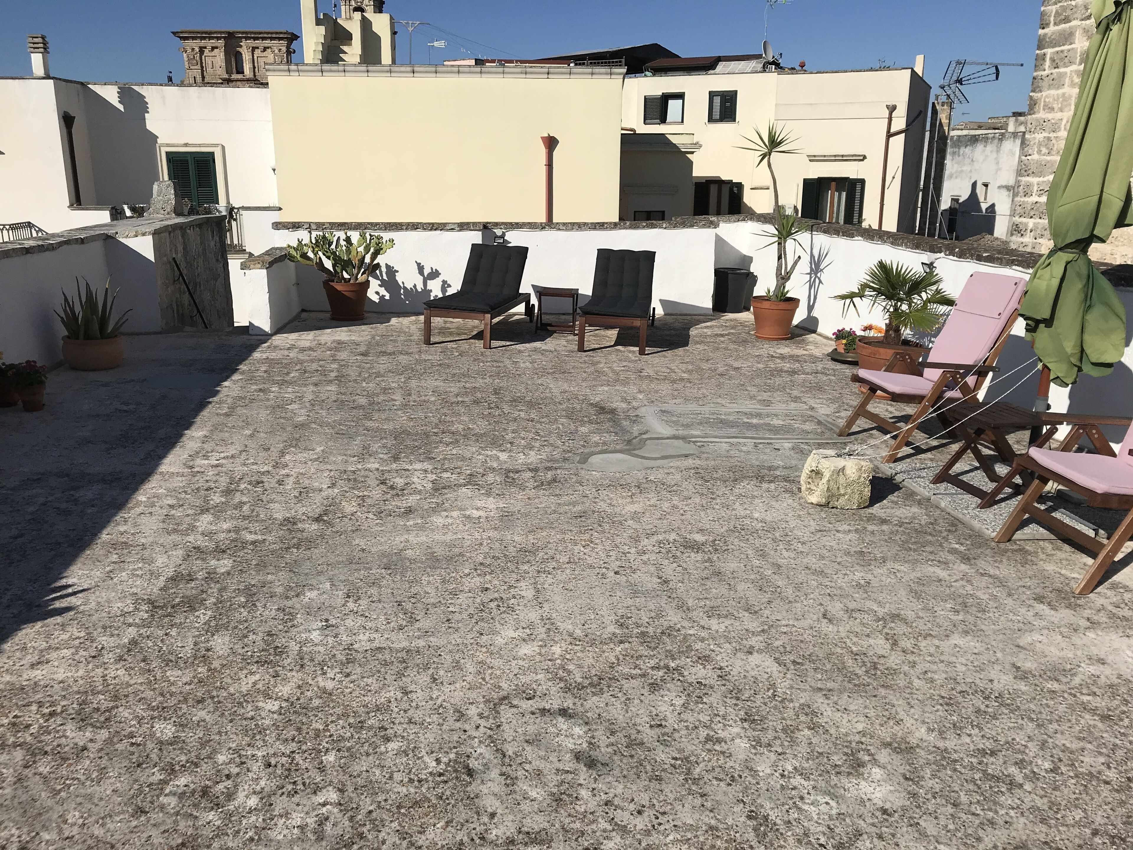A rooftop terrace with concrete flooring, potted plants, and wooden lounge chairs.