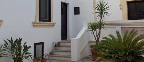 A courtyard with a white building, a staircase, and potted plants.