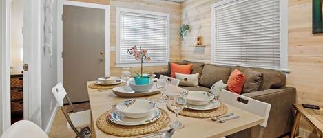 A modern dining area with a wooden table set for four, surrounded by white chairs.