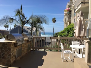 Un patio con una parrilla, sillas blancas y vista a la playa y al océano.