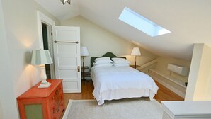 Une chambre à coucher comprenant un lit, deux tables de chevet avec des lampes, une commode, une lucarne et une armoire blanche.