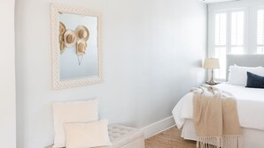 Ein Schlafzimmer mit weißer Wand, Holzboden, einem Bett mit weißer Bettwäsche, einem Nachttisch mit Lampe und einem Deckenventilator.