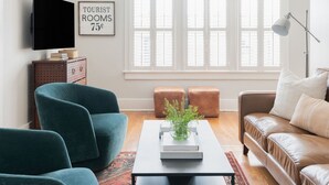 Ein modernes Wohnzimmer mit großem Fenster, Deckenventilator, Fernseher und Couchtisch mit dekorativer Vase.