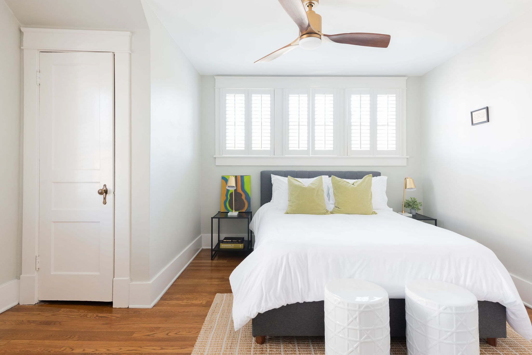 A bedroom with a large bed, a ceiling fan, a nightstand with a lamp, and a window with blinds.