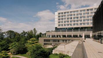 A modern building with a flat roof, large windows, and a paved courtyard with steps leading to the entrance.