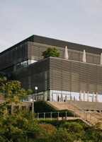 Un edificio moderno con fachada de diseño enrejado, ventanas amplias y una escalera que lleva a un nivel superior.