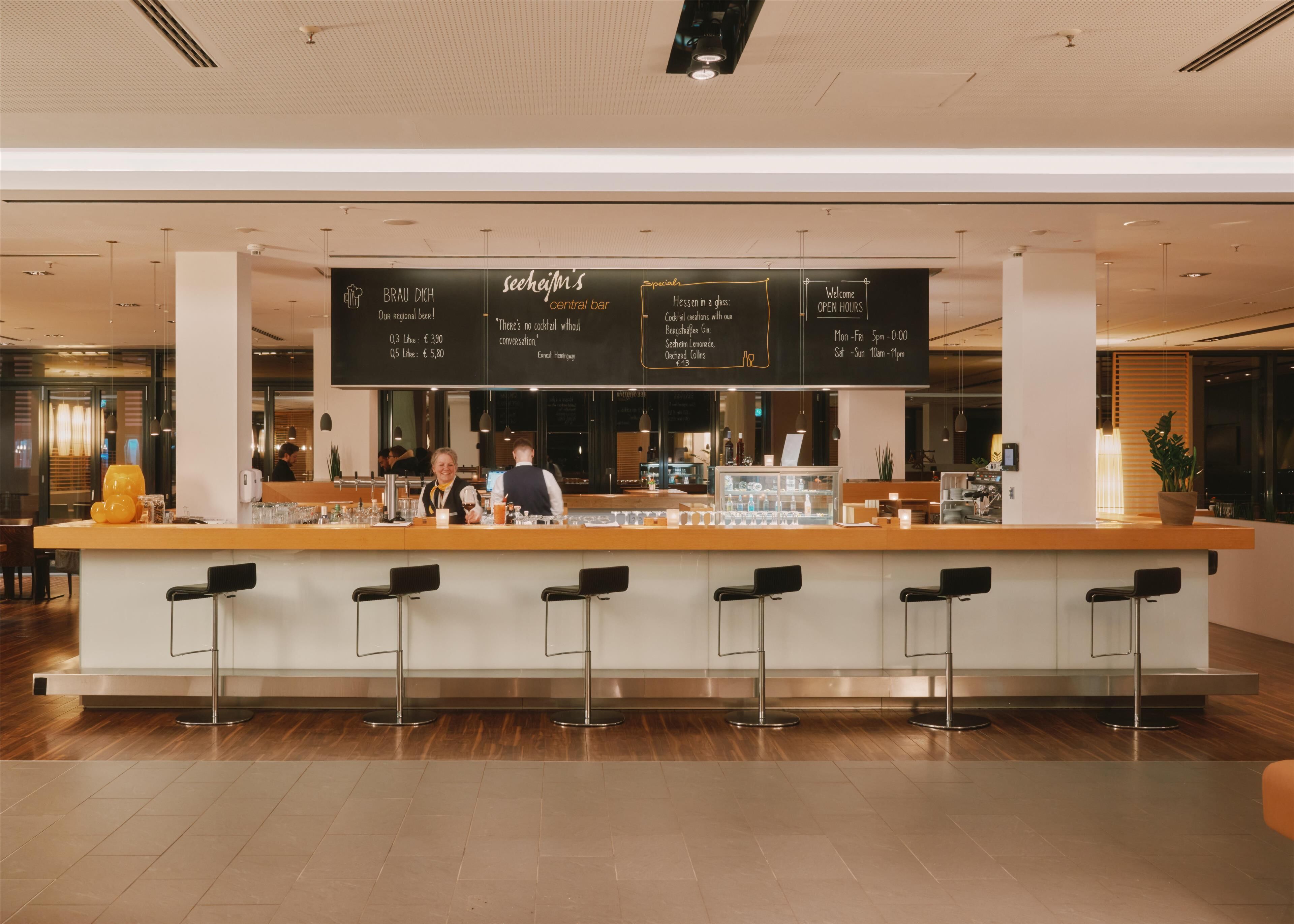 Un'area bar moderna con un bancone centrale, sgabelli e una lavagna con le offerte speciali e i prezzi.