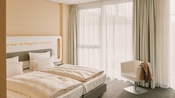 Ein Hotelzimmer mit einem Bett, einem Sessel und einem Fenster mit durchscheinenden Vorhängen.