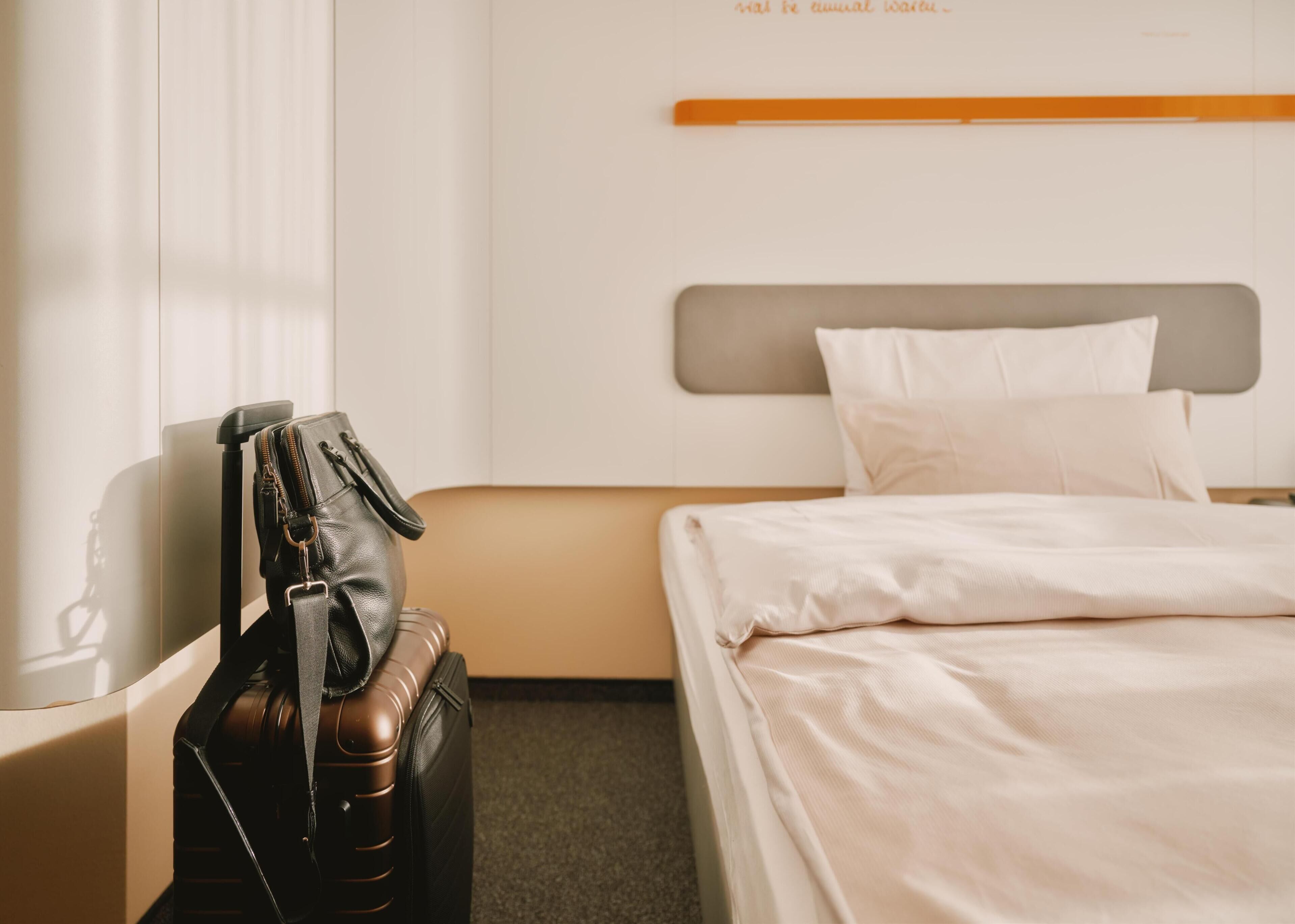 Una habitación de hotel con una cama, una maleta y un bolso sobre una mesita de noche.