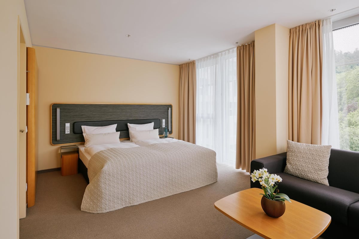 Une chambre d’hôtel avec un lit, un canapé, une table et une fenêtre avec des rideaux.