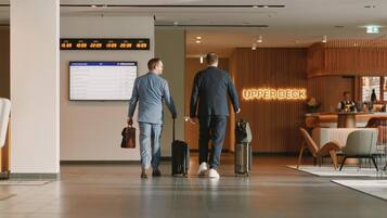 Un hall d’hôtel moderne doté d’un panneau d’affichage numérique indiquant les informations sur les vols, d’un comptoir d’accueil et d’un espace salon.