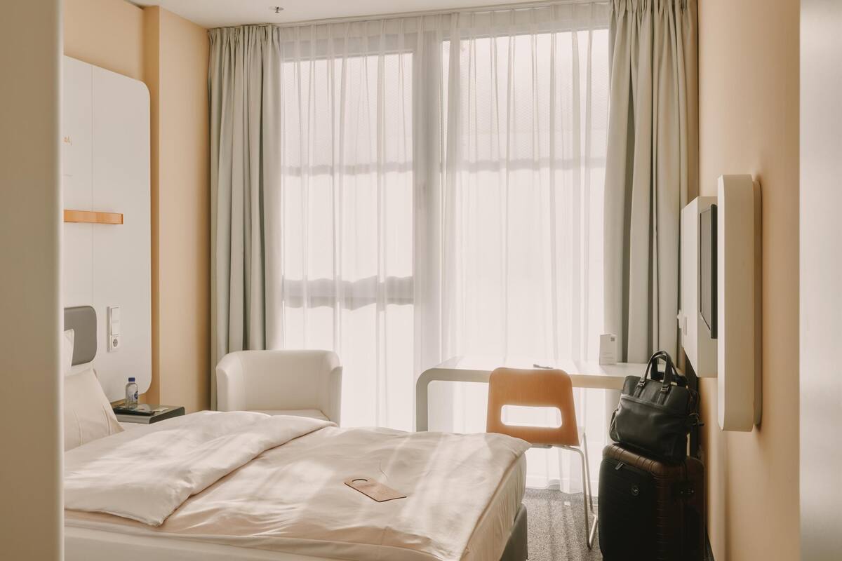 Une chambre d’hôtel avec un lit, une chaise, un bureau, une télévision et une valise.