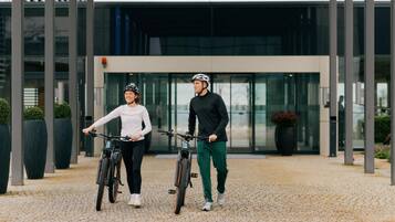 Two people on bicycles in front of a modern building with a glass entrance.