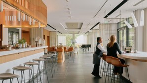 Un área de bar moderna con taburetes altos, una barra y un piano al fondo.