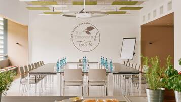 Une salle de conférence avec une longue table, des chaises, un tableau blanc et un mur orné d’un logo circulaire.