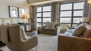 A modern living room with a sofa, armchair, and a small table with a lamp. Large windows offer a view of the cityscape. - Four Bedroom Penthouse in Canyons Village by RedAwning (Park City)