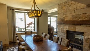 A long wooden dining table with chairs, a stone fireplace, and a view of a mountain through large windows. - Four Bedroom Penthouse in Canyons Village by RedAwning (Park City)