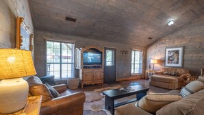 Ein gemütliches Wohnzimmer mit Holzbalkendecke, Ledersofas, einem Fernseher und einem Kamin.