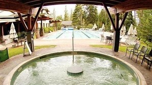 A circular hot tub with a central pole, surrounded by a tiled patio area with chairs and umbrellas. - Northstar Luxury Lodgepole 4 Bedroom Home by RedAwning (Truckee)