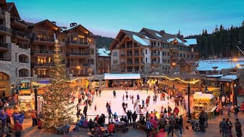 A bustling outdoor ice skating rink surrounded by multi-story buildings with balconies and large windows.