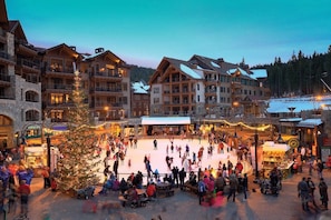 Skaters glide across the outdoor rink surrounded by historic buildings with balconies and large windows.