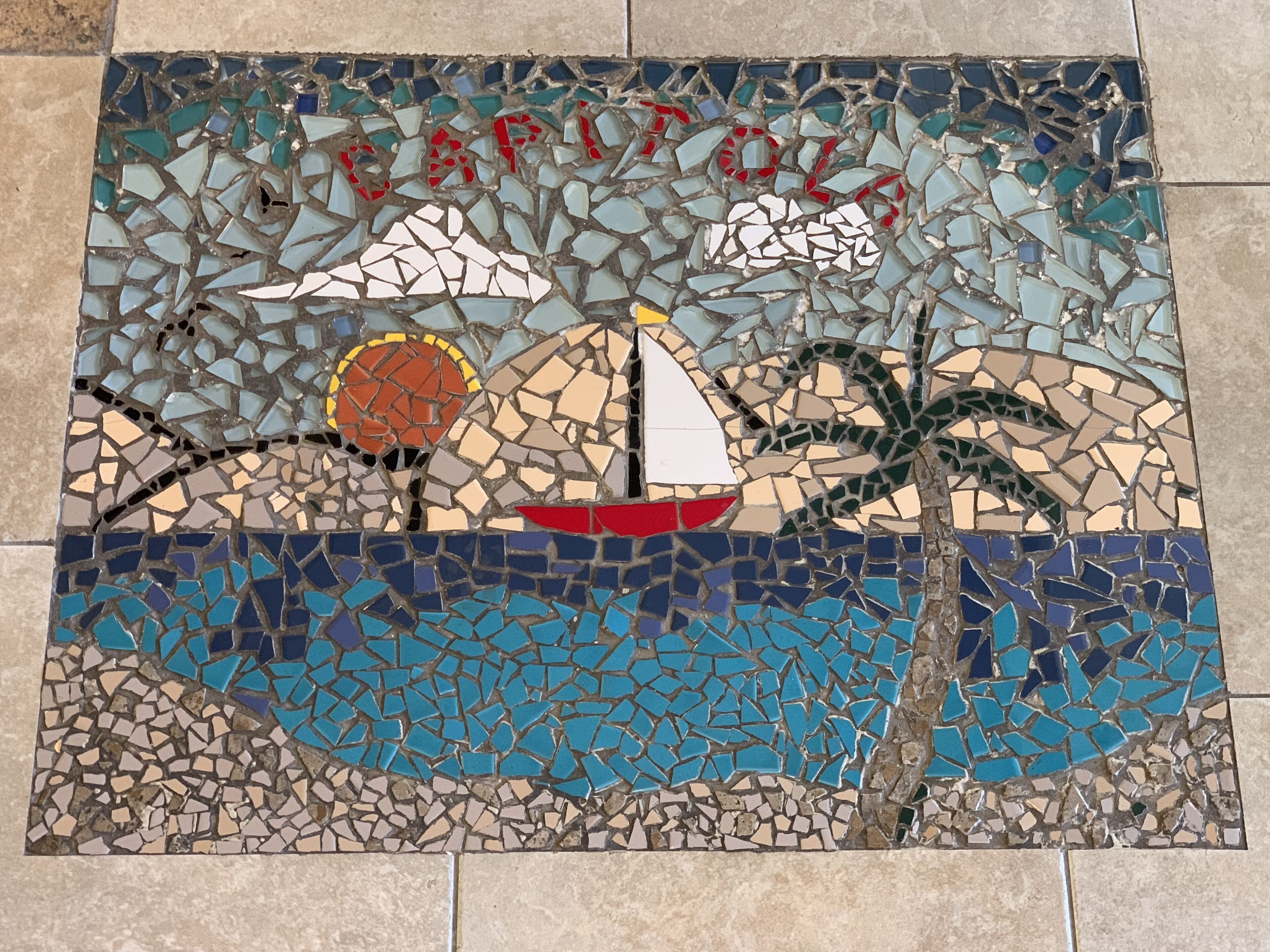 A mosaic tile with a sailboat, palm trees, and a sun.