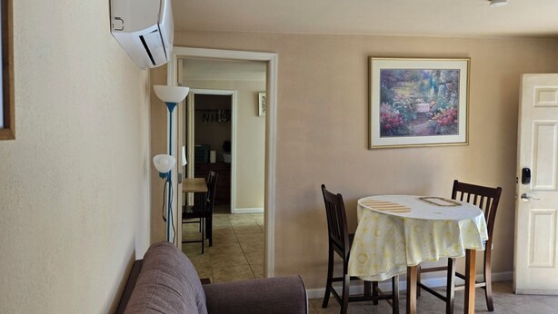 A living room with a sofa, a dining table with chairs, a painting on the wall, and an air conditioning unit.
