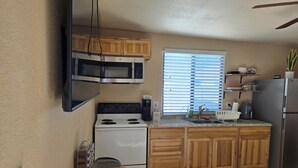 A kitchen with wooden cabinets, a stove, a microwave, a refrigerator, and a window with blinds.