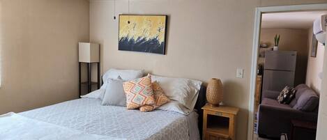 A bedroom with a bed, a ceiling fan, a bedside lamp, a small table, and a painting on the wall.