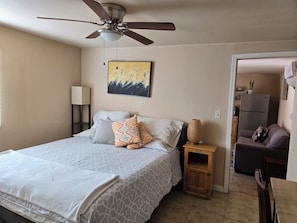 Une chambre à coucher avec un lit, un ventilateur de plafond, une lampe de chevet, une petite table et un tableau au mur.