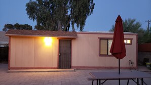 A small building with a wooden door and a window, a red umbrella, and a picnic table.